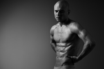Fototapeta premium Muscular man posing in a dramatic black and white scene, showcasing strength and determination with a powerful expression and artistic lighting.