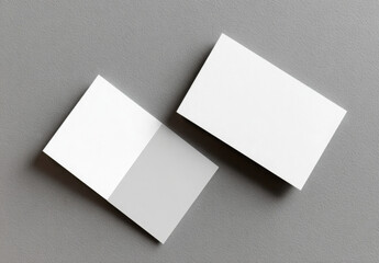 Top-down view of two blank white business cards, one folded and one closed, on a gray background.