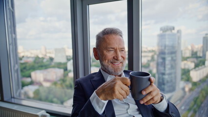 Fototapeta premium Wealthy executive holding coffee cup sitting by office panoramic window closeup.