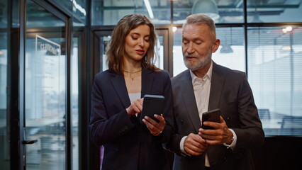 Office managers discussing project on go corridor holding smartphones closeup.