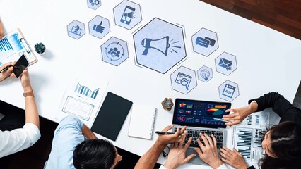 A diverse business team collaborates on digital marketing strategies, analyzing data on laptops surrounded by various communication icons and performance charts. Raster