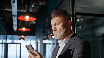 Senior entrepreneur watching mobile phone in office building corridor closeup.