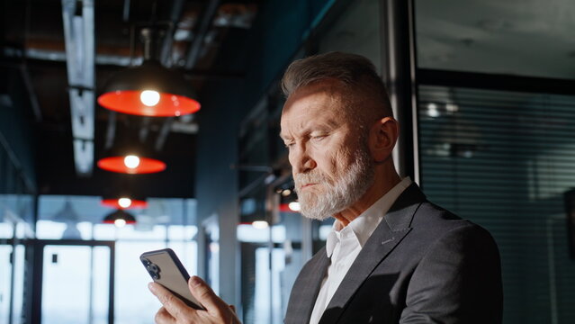 Senior entrepreneur watching mobile phone in office building corridor closeup.