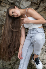 Beautiful woman in a white top and gray jeans poses on rocks in the mountains