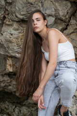 Beautiful woman in a white top and gray jeans poses on rocks in the mountains