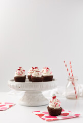 Brownie Rounds Frosted with Vanilla Buttercream and Valentine Sprinkles; One in Front on Valentine's Day Napkins; More on White Pedestal in Background with Milk Bottle; Copy Space