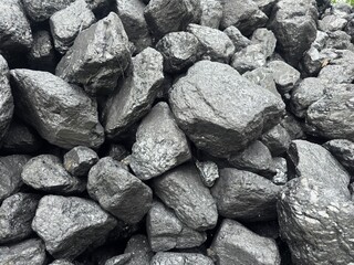 A large, dense pile of rough, dark gray and black coal lumps fills the frame, showcasing the rock's irregular shapes and texture.