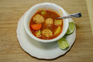 A white bowl of turkey albondiga soup with lime wedges on the side.