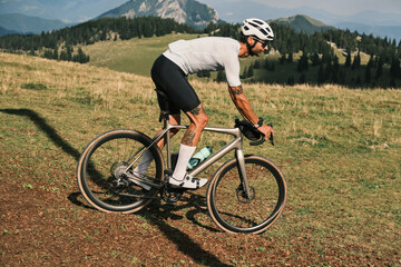 Fototapeta premium Cyclist on gravel road through scenic mountain landscape. Epic adventure, freedom, and exploration theme. Perfect for travel, sports, or outdoor lifestyle projects.