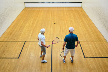 Elderly couple plays squash in vibrant court, demonstrating active lifestyle, fitness, and joy of sport in later years.