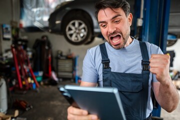Excited mechanic celebrating good news on tablet in auto repair shop