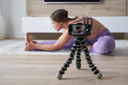 Young female blogger recording sports video at home doing yoga in living room - Powered by Adobe