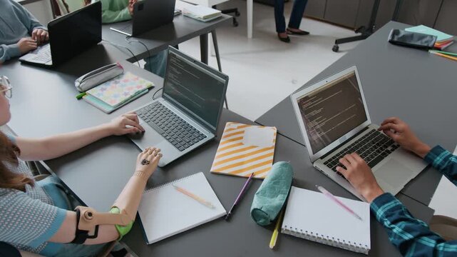 High angle shot of unrecognizable girl with prosthetic arm using laptop along with her classmates during programming lesson in school
