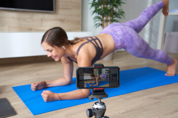 Young female blogger recording sports video at home doing yoga in living room with laptop