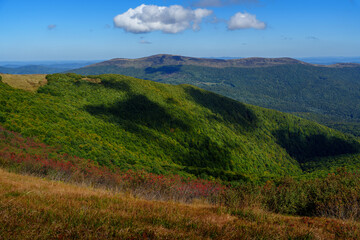 White clouds casting shadows on forested mountain ridges under bright blue sky