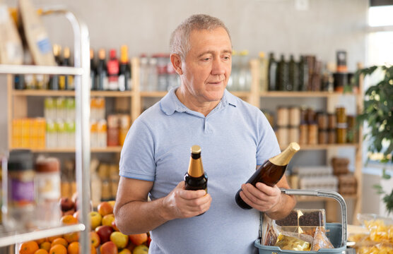 Concerned old man is deciding between kinds of beer in the supermarket
