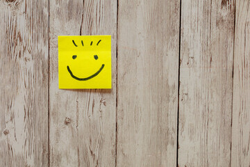 Yellow sticky note with smiley face on wood