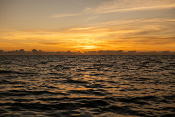Obraz premium Golden sunrise in Itacaré, Bahia, Brazil. Boats floating on calm sea, yellow light on the horizon, tropical coastal landscape with warm tones and natural beauty.