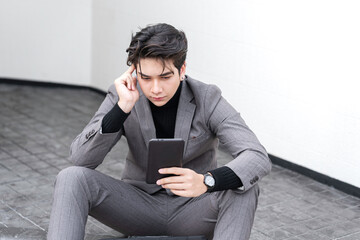 Young businessman sitting outdoors using smartphone with briefcase