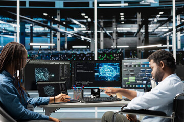 Data center engineer in wheelchair and coworker using AI visualization to oversee automated tasks. Worker with disability in inclusive server farm and colleague modifying systems based on analytics