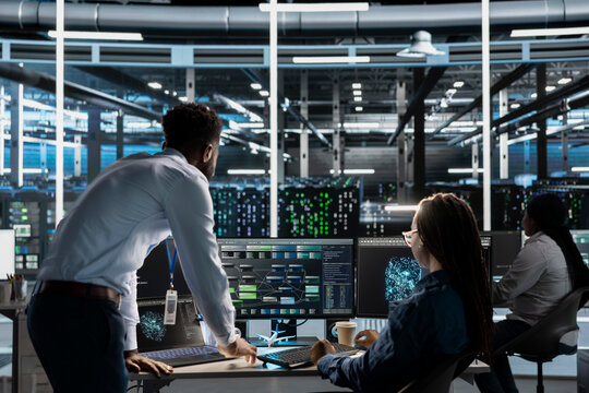 Data center manager supervises engineer using AI visual programming to optimize gear. Server farm team leader overseeing work done by worker colleagues using artificial intelligence analysis software