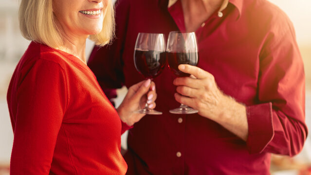 Affectionate senior couple toasting with red wine while cooking festive dinner at kitchen. Elderly man and his wife drinking alcohol, having romantic moment, preparing holiday meal at home