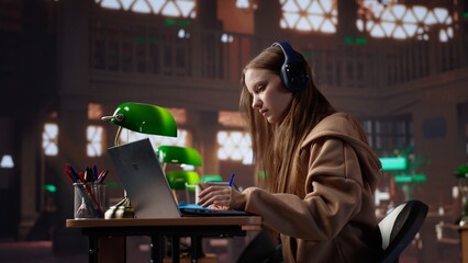 Young girl listening to educational documentary on laptop and takes notes, using modern non...