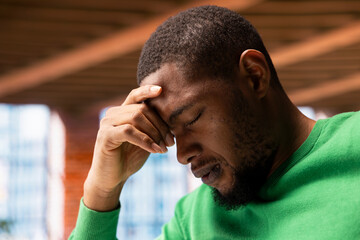 Upset man shaking head in disbelief, feeling upset by events while staying at home. Dejected african american person closing eyes in apartment, left speechless by troubling news