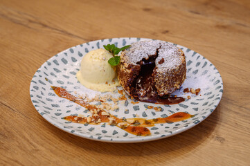 Chocolate lava cake with vanilla ice cream, crushed nuts and powdered sugar, artistically plated on dotted ceramic plate on wooden table in cozy restaurant.