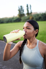 Vertical. Young female athlete enjoying a refreshing drink from a reusable bottle after an intense...