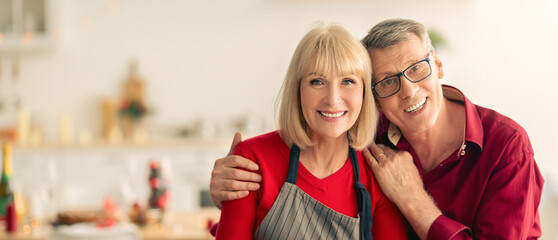 Loving Caucasian senior couple making Thanksgiving or Christmas dinner together, smiling at camera, cooking traditional meal for family celebration at kitchen, copy space