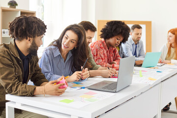 Team of young diverse multiracial people sitting at office table, working on their business projects, discussing ideas, developing marketing plans, and using laptops