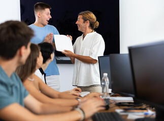 Happy excited young guy receiving offer to join group of developers at promising IT startup. Friendly male project manager giving him official contract