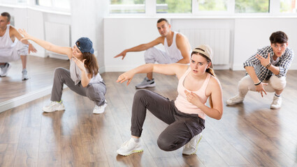 Obraz premium Active young girl performing seated pose of breakdance in training hall during dancing classes
