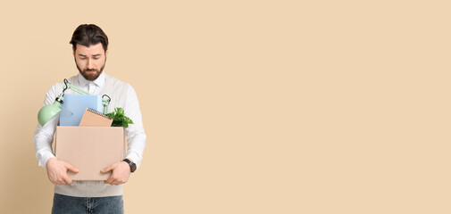 Fired young man holding box with personal stuff on beige background