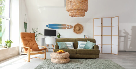 Interior of light living room with sofa, workplace and hanging surfboard