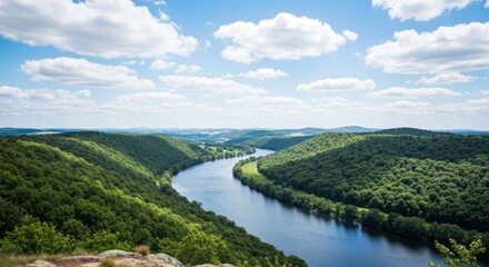 Fototapeta premium High-angle view of a meandering river flowing through lush green valleys and hills. Vast landscape stretches beneath a partly cloudy sky