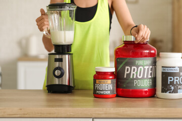 Sporty young woman making protein shake in blender at home, closeup