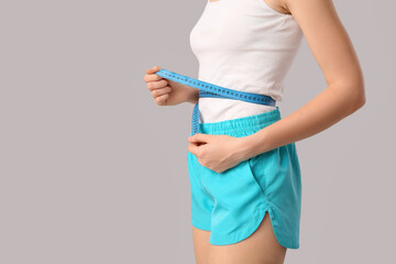 Sporty young woman with measuring tape on grey background. Weight loss concept