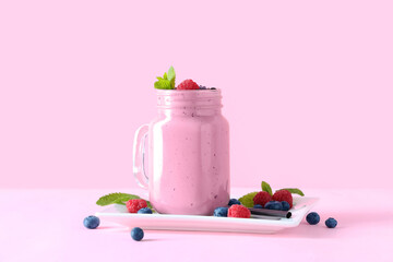 Mason jar of fresh smoothie with blueberries and raspberries on pink background