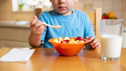 Child eating healthy breakfast with fresh fruit salad and milk, promoting nutritious eating habits for toddlers and cheerful family mealtimes