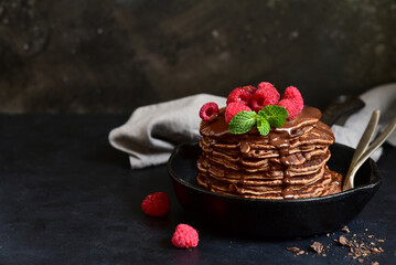 Chocolate banana pancakes with sauce and raspberries on a skillet  .