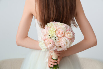 Beautiful bride with wedding bouquet on light  background, back view