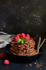 Chocolate banana pancakes with sauce and raspberries on a skillet  .