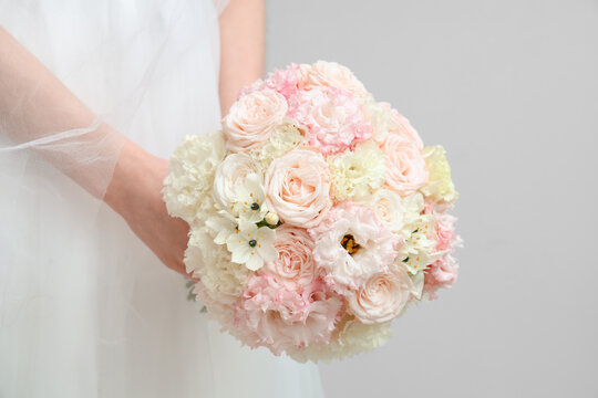 Beautiful bride with wedding bouquet on light background, closeup