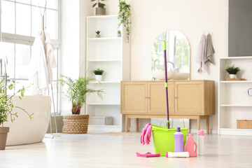 Mop with bucket and different cleaning supplies on floor at home