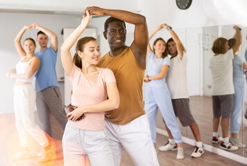 Naklejka premium Joyful active adult men and women learning to dance in pairs in modern choreographic studio, indoors