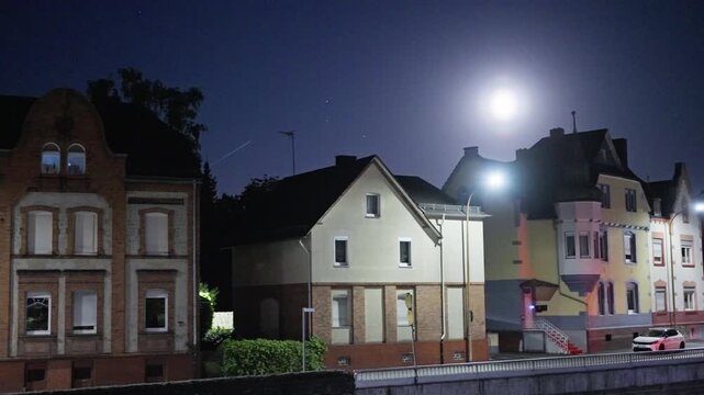 A serene night view of urban houses illuminated by a bright moon, showcasing the nighttime street lighting. Germany. Herborn city