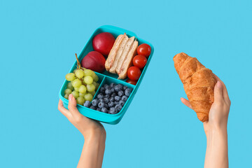 Female hands with school lunch box and croissant on blue background