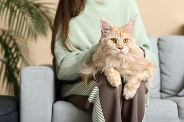 Young woman sitting on sofa with cute Maine Coon cat at home